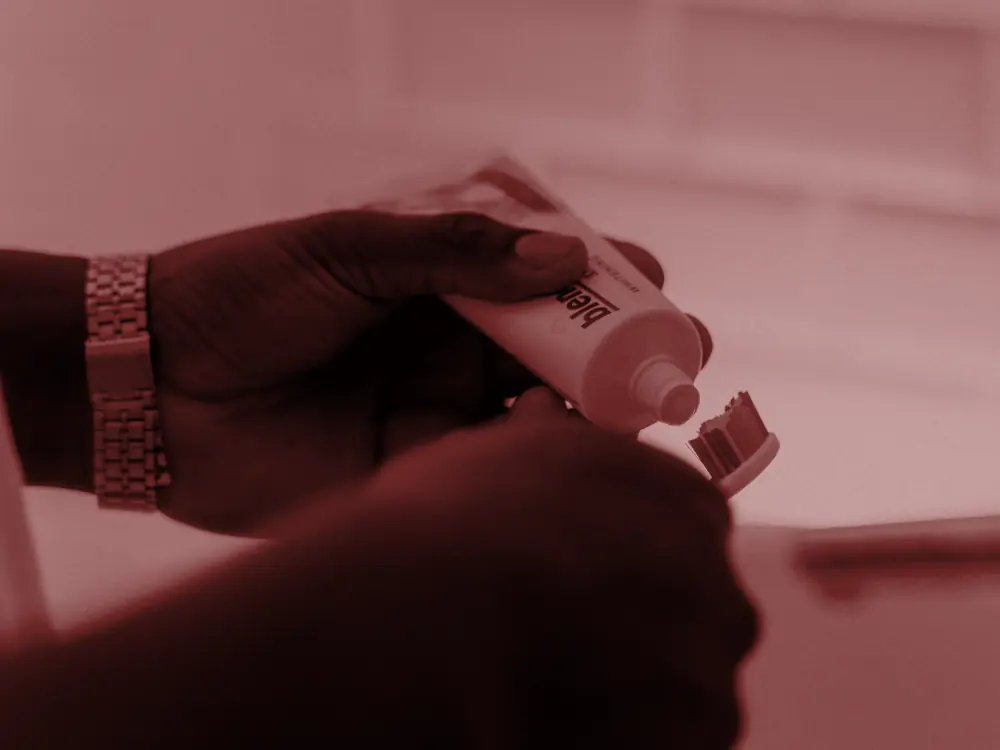 Hands squeezing toothpaste onto a brush, black and white